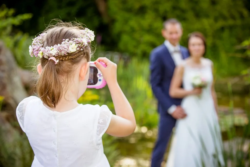 Blumenkind fotografiert das Brautpaar im Hintergrund